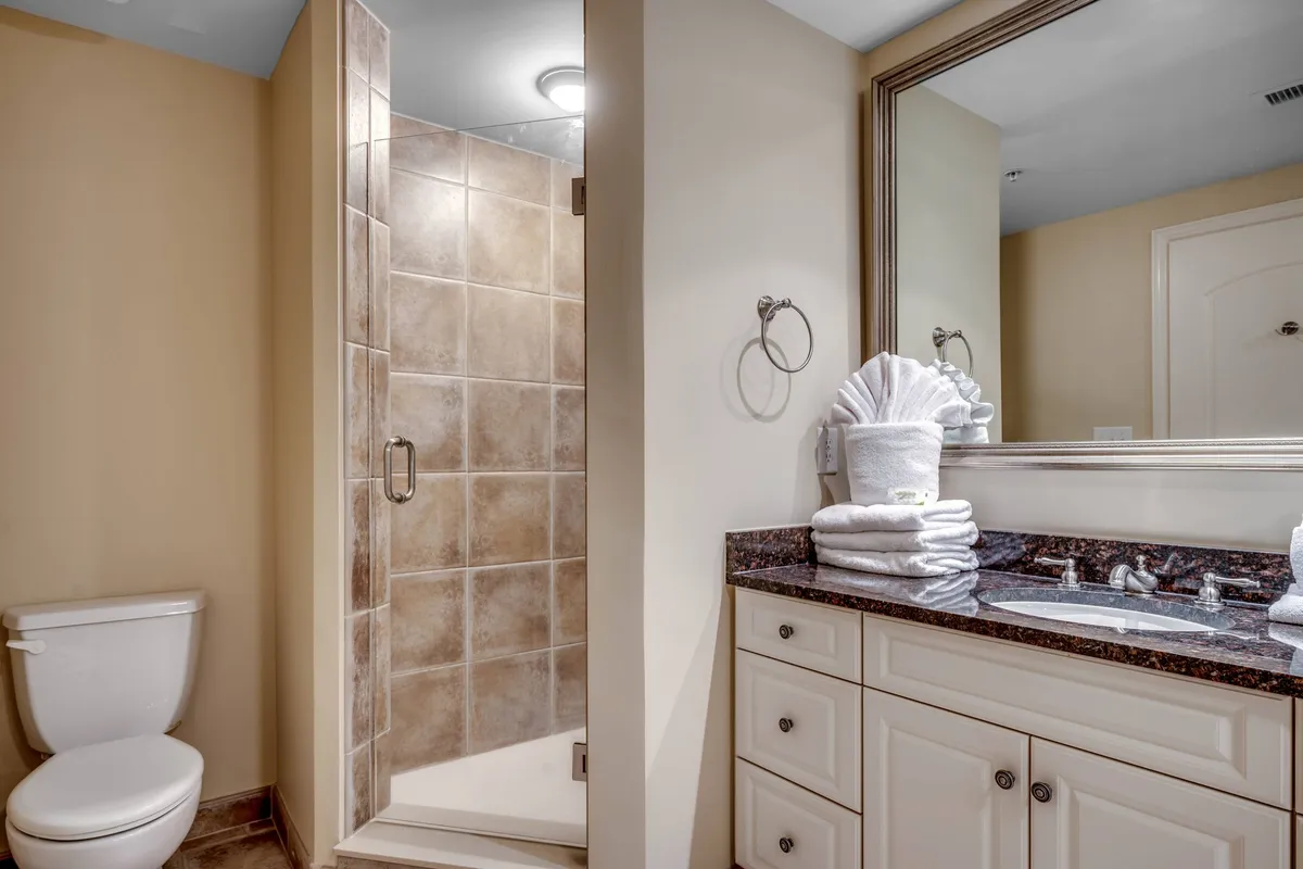 This bathroom features a glass-enclosed shower, a vanity with a sink, a large mirror, and neatly arranged towels. The setting is modern and inviting, ideal for refreshing after a day in the sun or preparing for restful sleep.