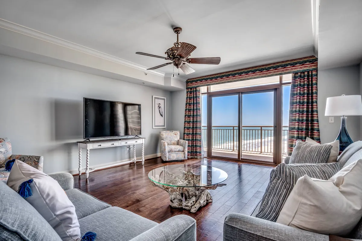 The image showcases a spacious and inviting living room with a modern, comfortable seating area. Large glass windows frame breathtaking ocean views, allowing natural light to flood the space. A sleek television and a stylish coffee table suggest a perfect spot for family game nights or relaxing movie evenings. The serene atmosphere hints at quiet mornings with a book while overlooking the water from the balcony.