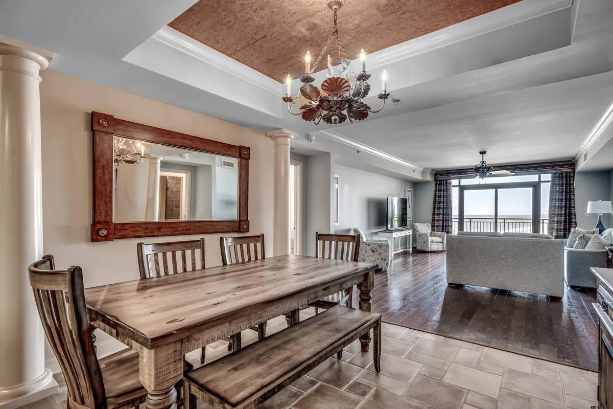 Featuring a dining table beneath an elegant chandelier and a large window with sunset views, this image radiates warmth and togetherness. The layout encourages family gatherings, meals, and game nights, while the inviting atmosphere makes it easy to imagine sharing stories into the evening.