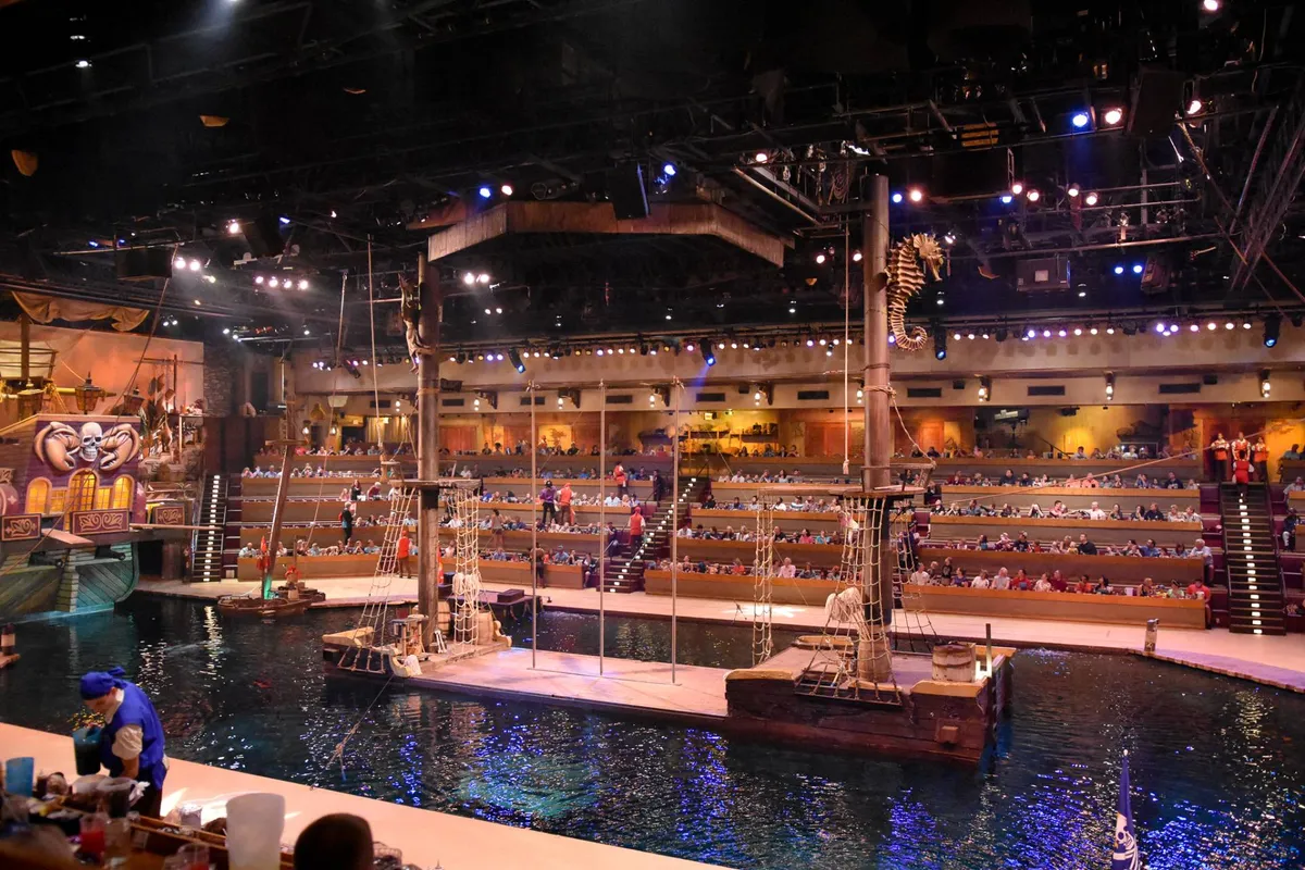 This image showcases a vibrant staging area designed for live performances, complete with an audience seating area and immersive themed decorations around a water feature. The setup evokes the ambiance of dinner shows and interactive entertainment, echoing the exclusive access to attractions like Pirate’s Voyage mentioned in the section.