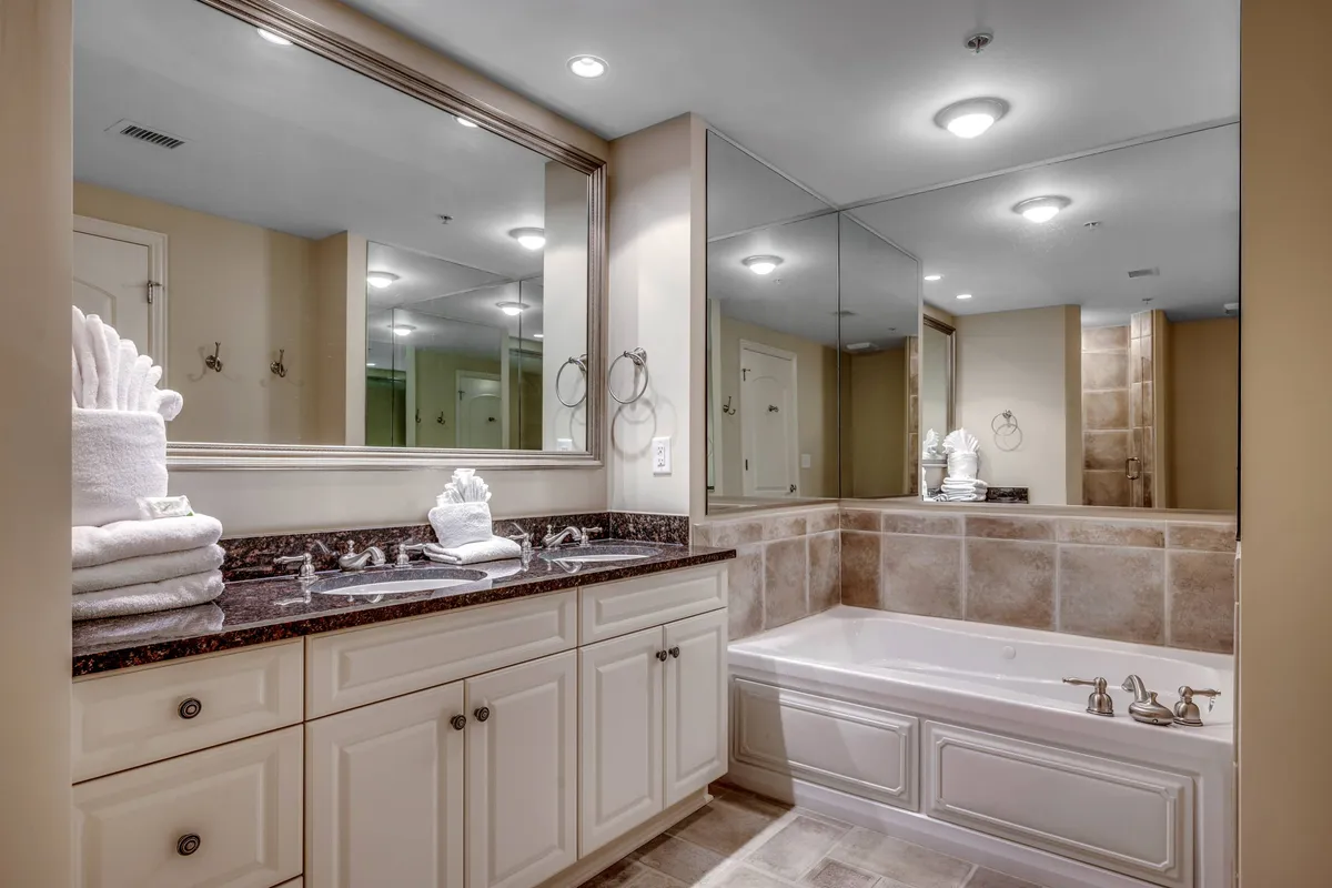 A tranquil spa-like bathroom interior featuring a deep soaking bathtub, a mirrored wall, and a plush vanity with neatly stacked towels. The serene mood is ideal for illustrating moments of self-care, pampering, and rejuvenation.