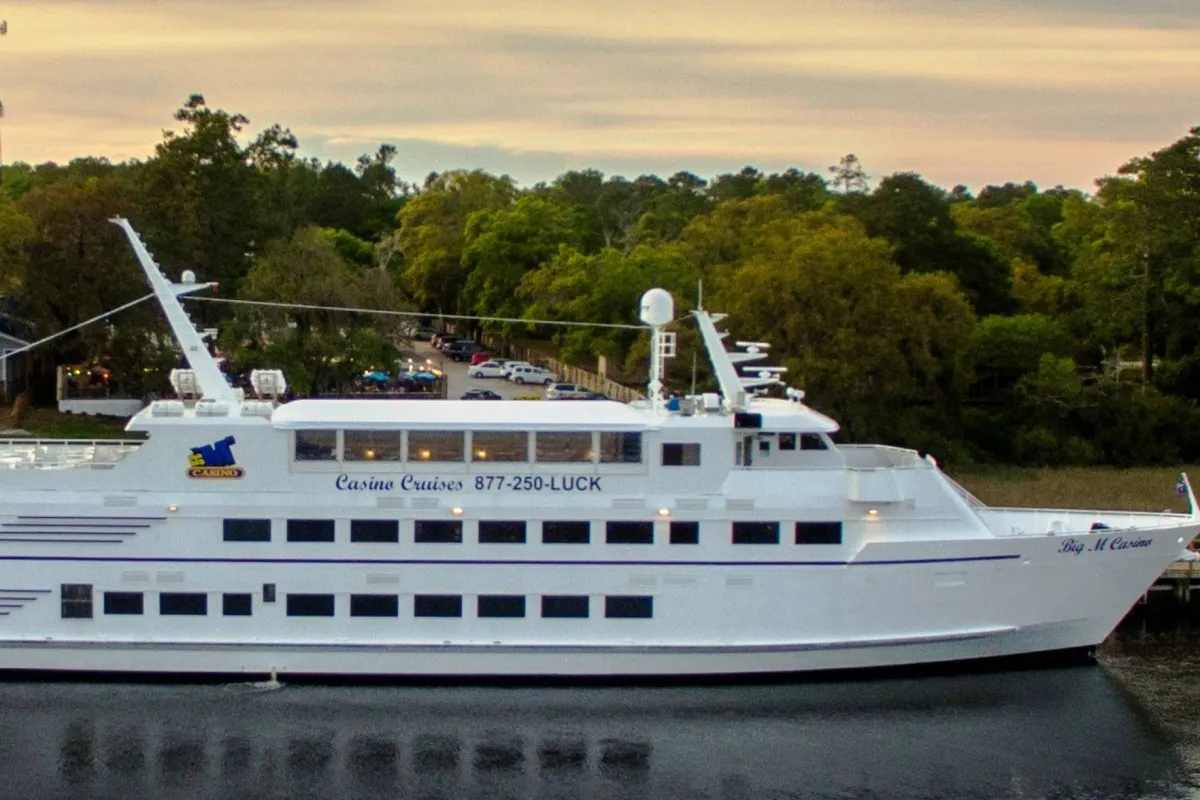 This image features a luxurious yacht docked on calm waters, surrounded by lush trees, capturing the excitement of riverboat experiences. The scene hints at premium dining, sunset views, and exclusive entertainment options such as those included in the local attractions package.
