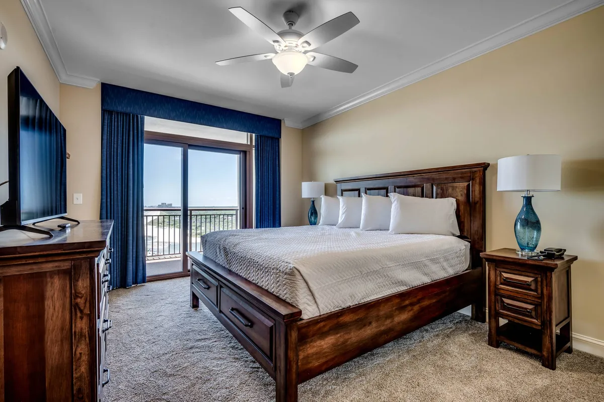 This image features a serene bedroom with a king-sized bed positioned near a large window, allowing natural light to flow in. Wooden furniture adds warmth, and a television is visible for in-room entertainment. The overall atmosphere is calm and inviting, perfect for relaxation.